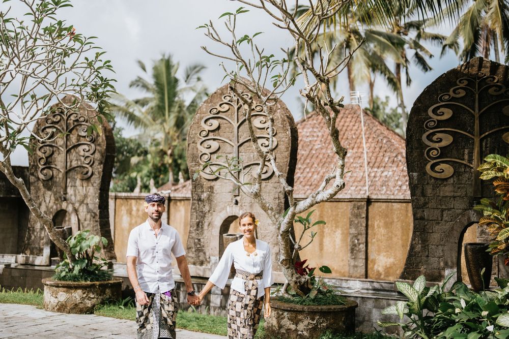 Two people walk hand in hand through lush tropical gardens with palm trees.