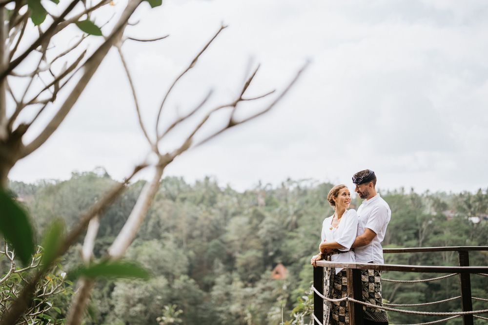 A couple poses on an outdoor deck with traditional Balinese stone sculptures visible.