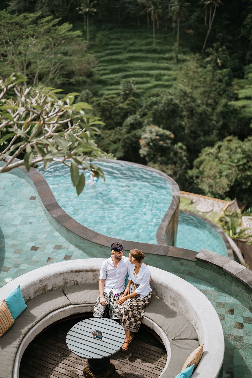 Couple relaxing on curved seating area overlooking tropical infinity pool.