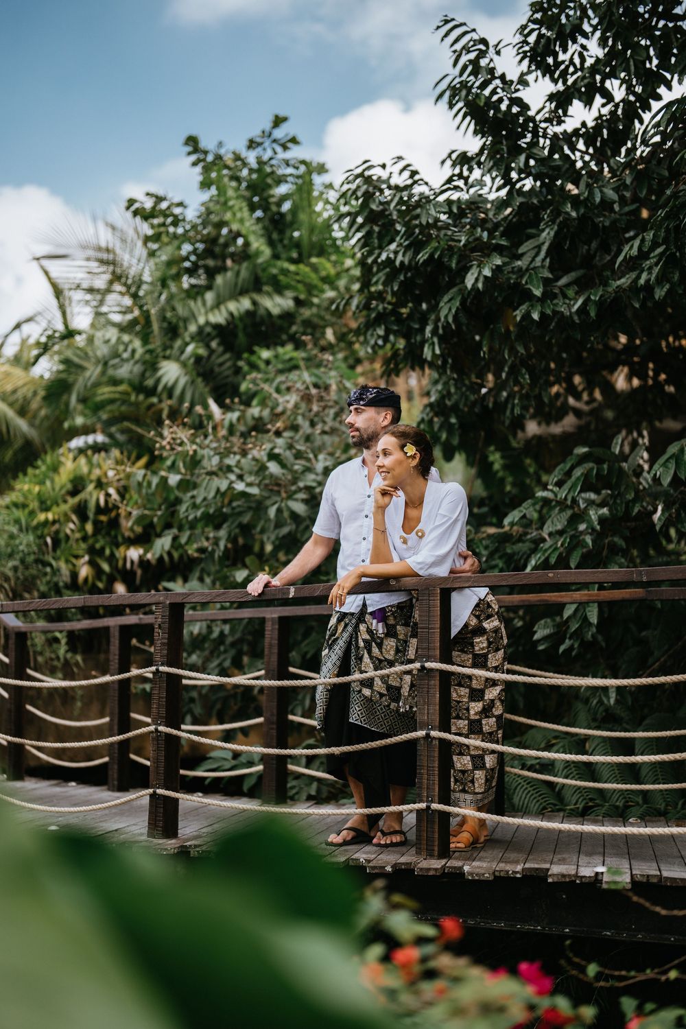 Couple sharing moment on wooden bridge surrounded by lush tropical gardens.