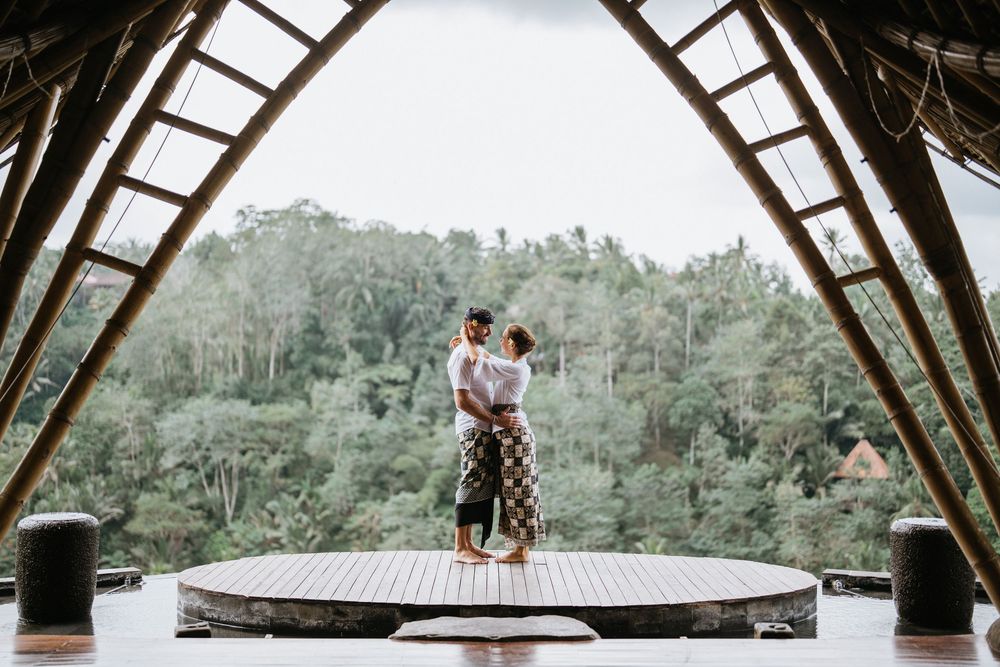 Wide angle view of bamboo roof structure with couple silhouetted against tropical landscape.