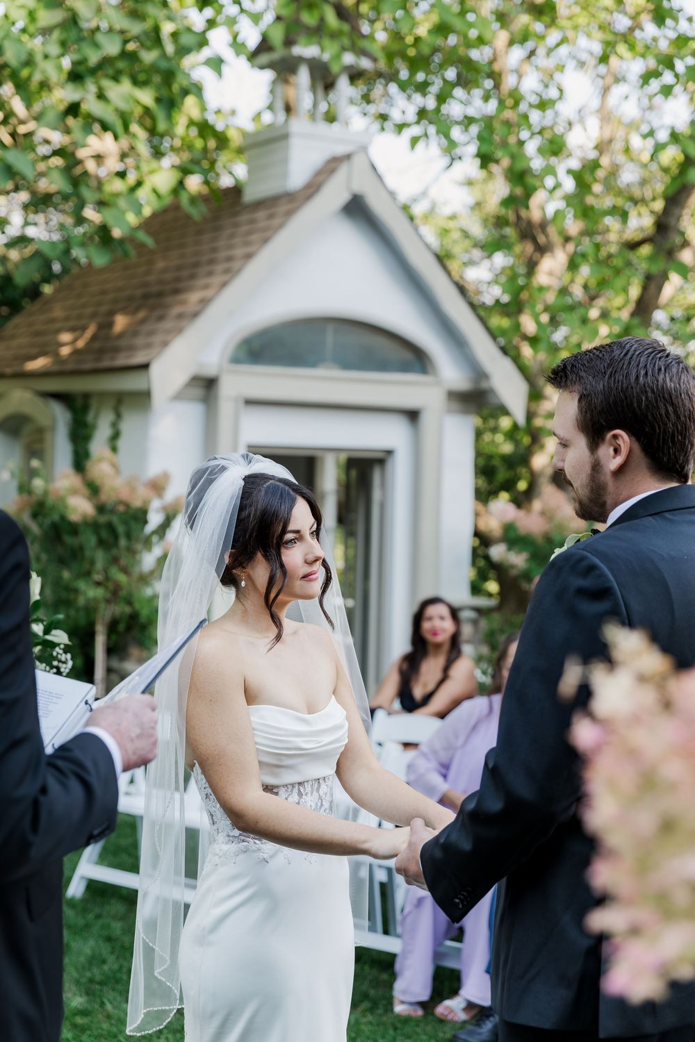 Garden wedding ceremony in front of a charming white chapel with spring blossoms at The Wren House in St. Jacobs, Ontario.