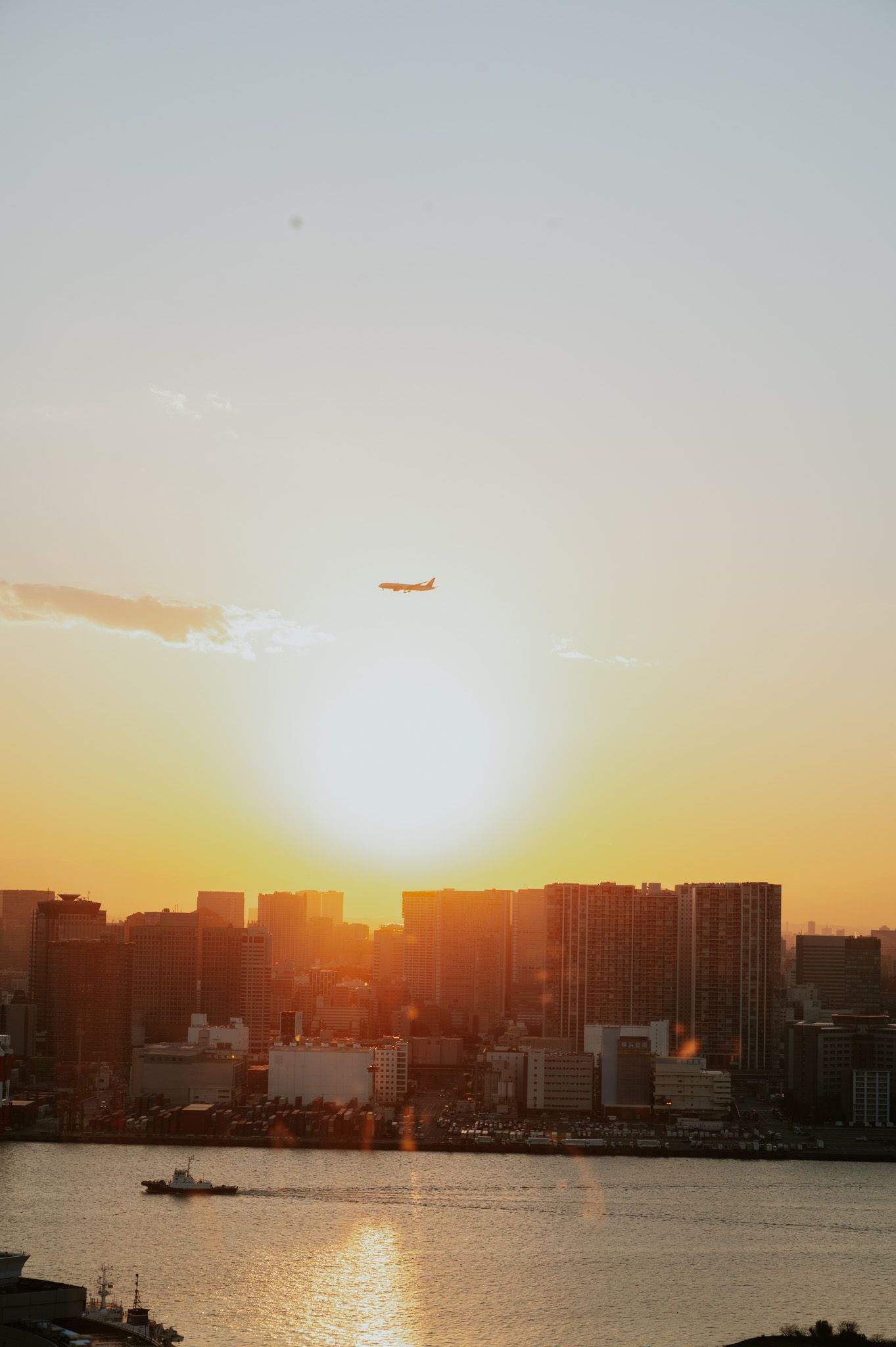 Beautiful sunset over Tokyo skyline with silhouetted buildings and orange sky reflecting on the harbor waters.