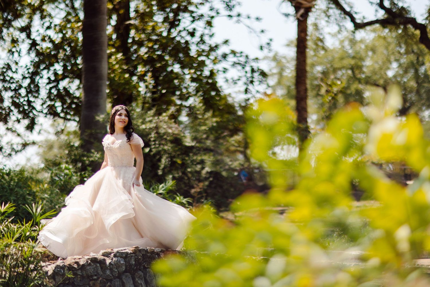 A flowing white wedding dress twirls in a sunlit garden setting.