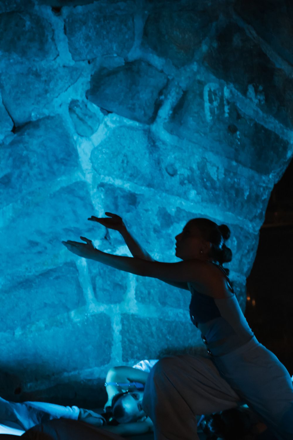 Silhouettes of dancers against a dramatic blue cave-like background.