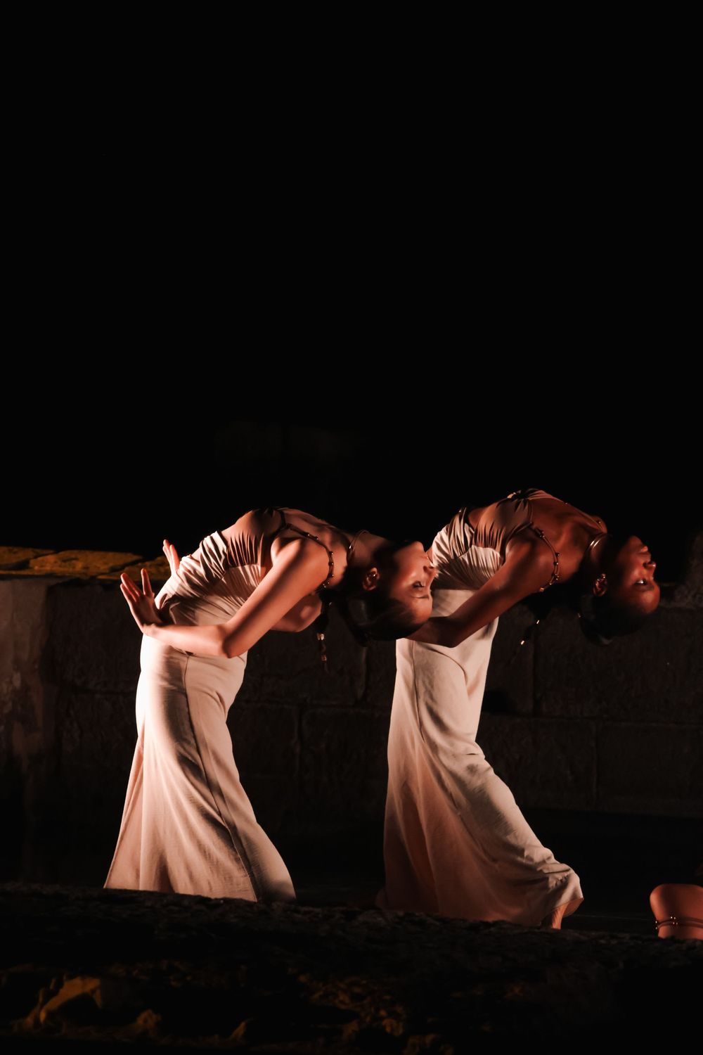 Dancers in white costumes performing expressive movements on a dark stage.