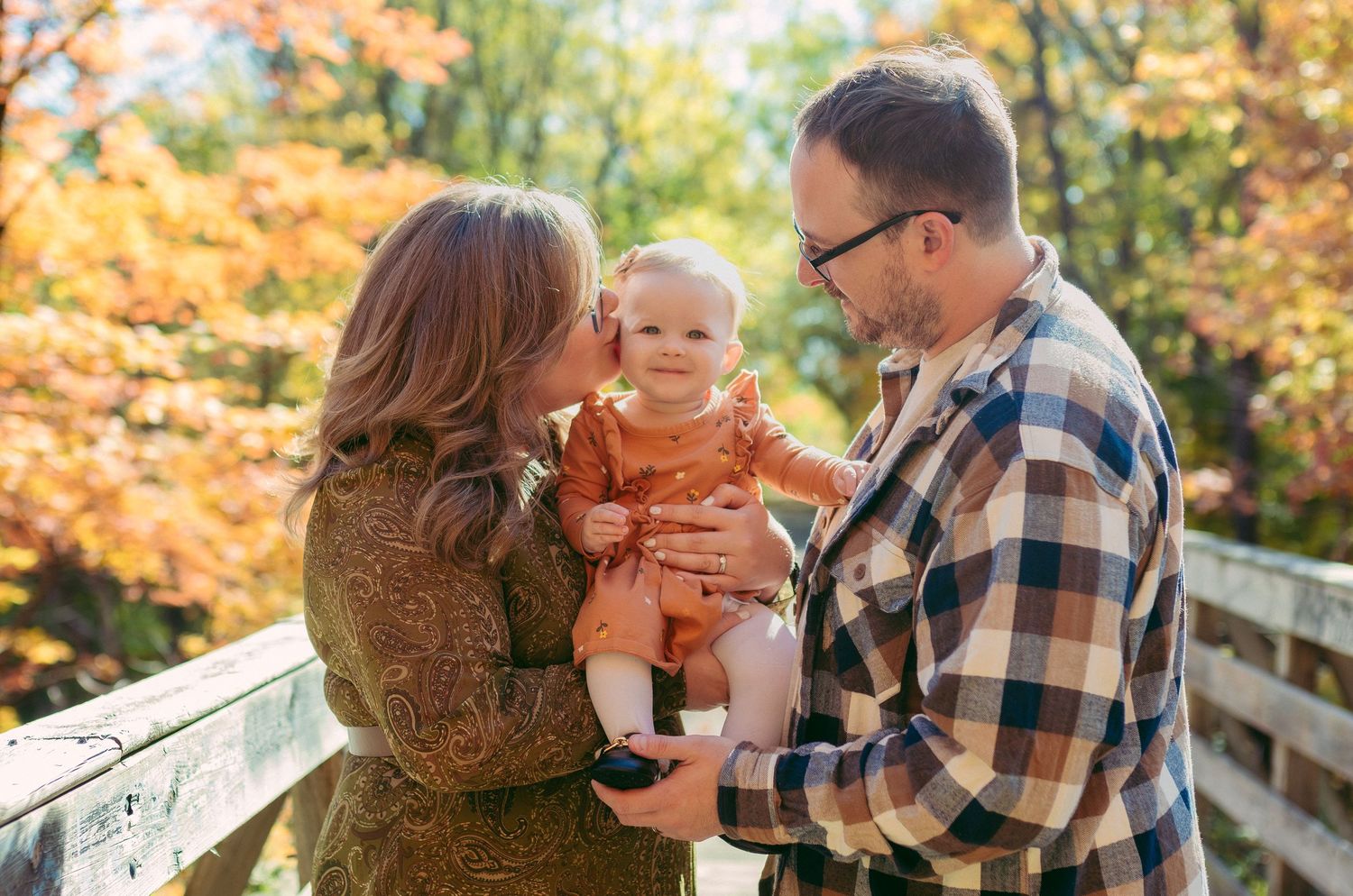 A family shares a joyful moment together on a wooden bridge surrounded by vibrant autumn foliage.