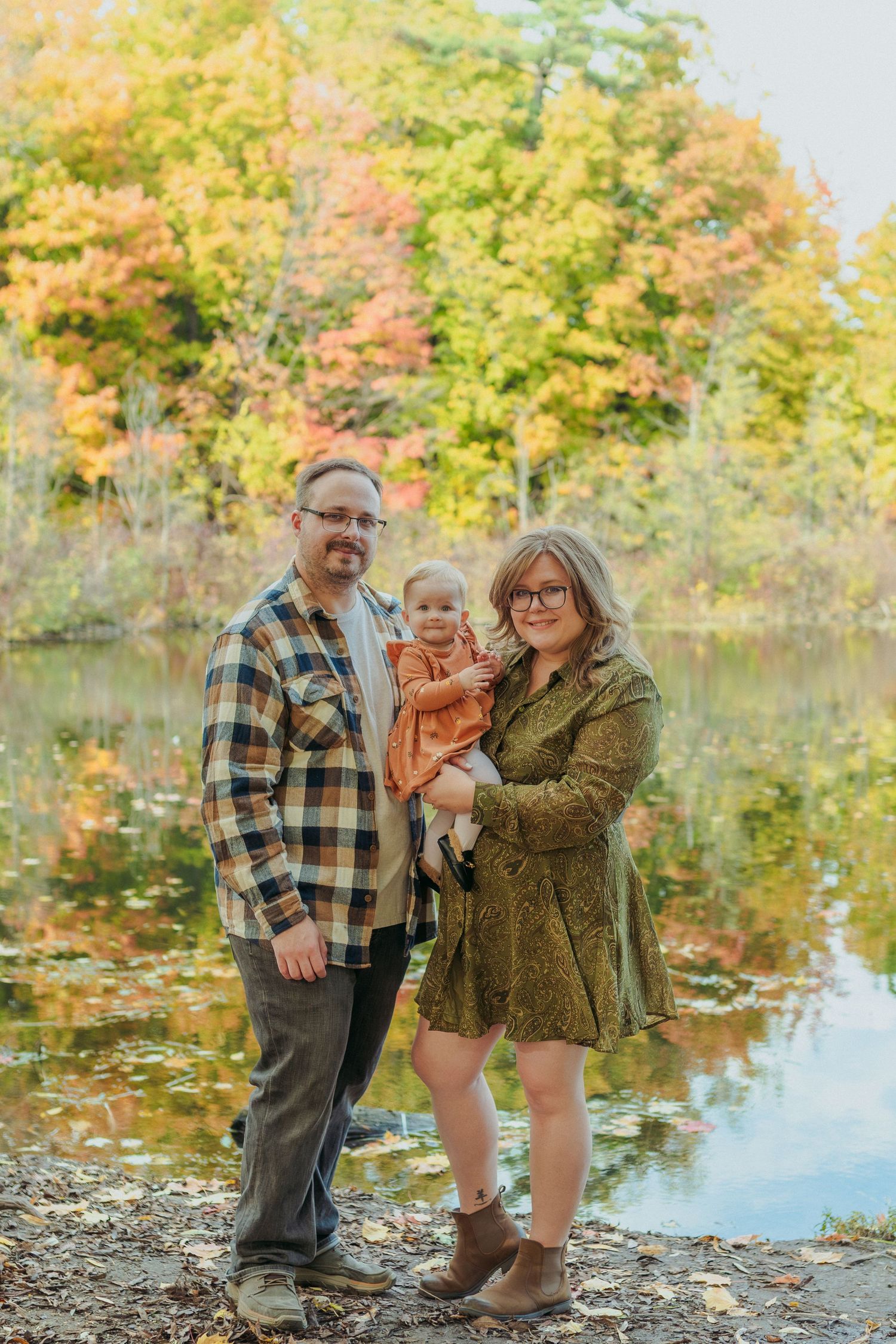 Family enjoying autumn scenery by a lake with colorful fall foliage reflected in the calm water.