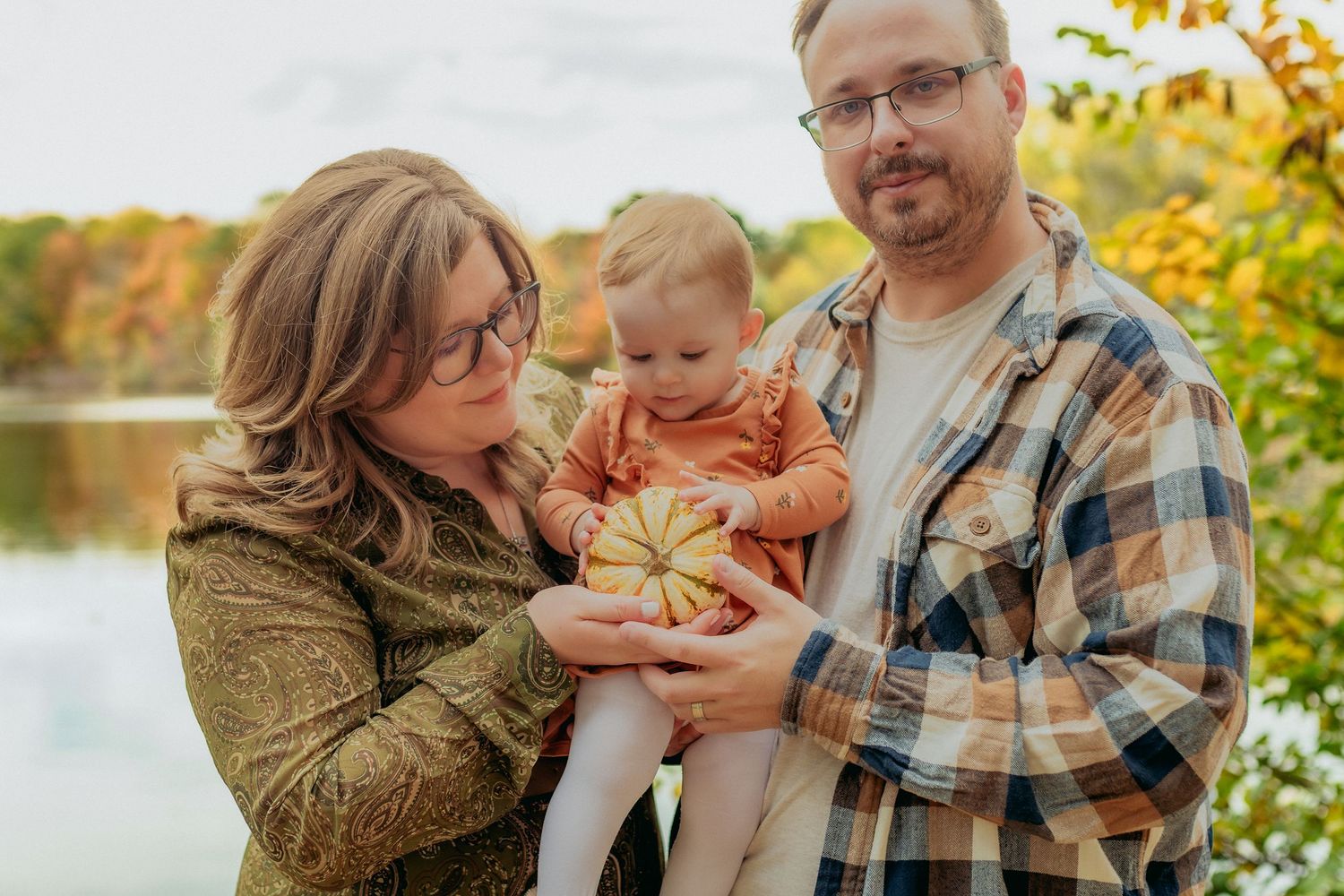 Family poses together in a natural outdoor setting with golden autumn light filtering through trees.