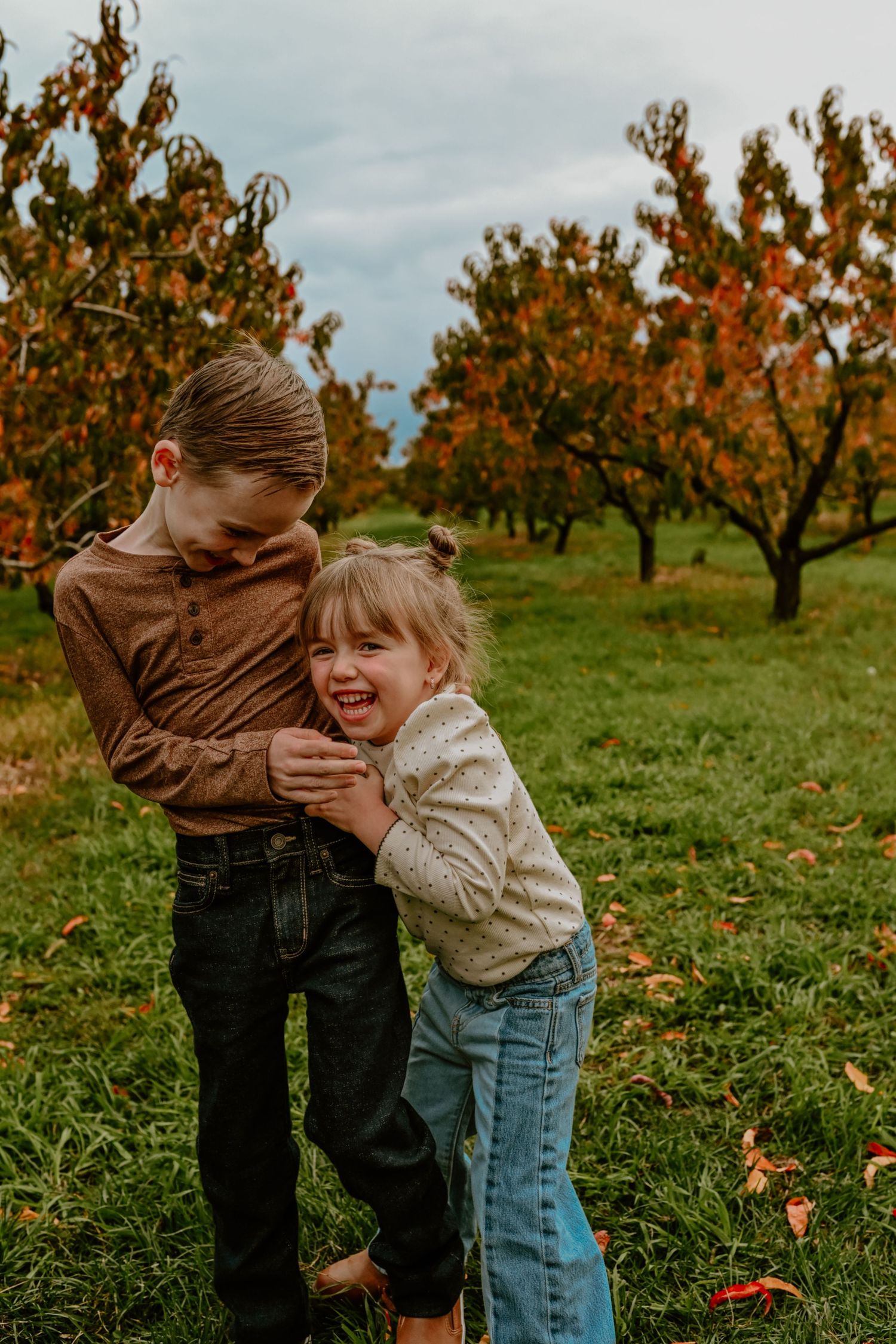 Two people share a playful moment together in an autumn orchard with orange trees in the background.