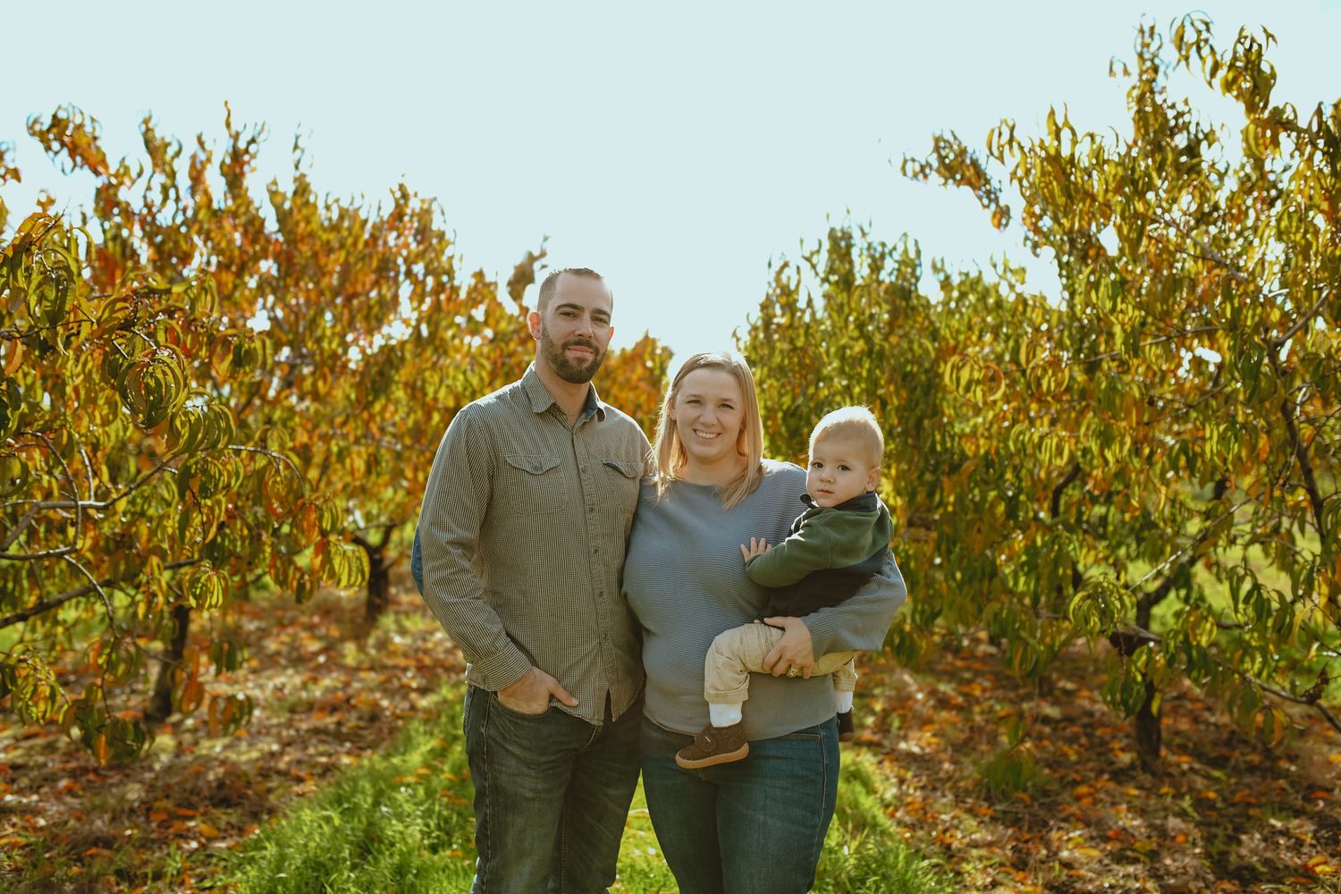 A group enjoys a sunny autumn day together in an apple orchard with golden leaves and trees in the background.