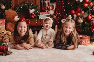 Three children lying on carpet surrounded by Christmas decorations and teddy bears.