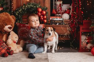 Child sitting with small dog surrounded by teddy bears and Christmas decorations.