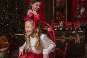 Two people sharing laughter during Christmas photo session with toy train and festive decorations.