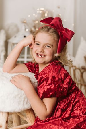 A festive holiday portrait featuring a red velvet dress and matching bow against a sparkly backdrop.