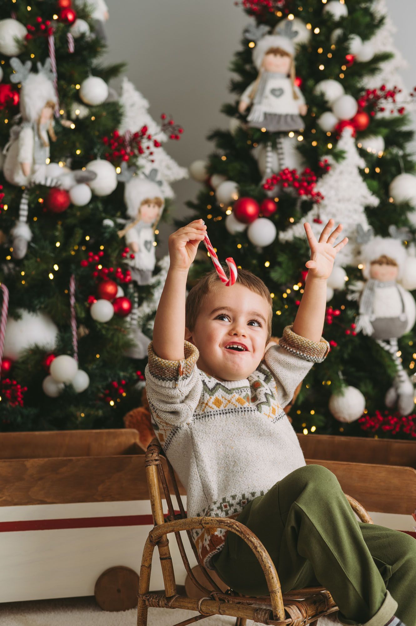 Child in a sweater reaches up excitedly in front of a decorated Christmas tree with angel ornaments and white baubles.