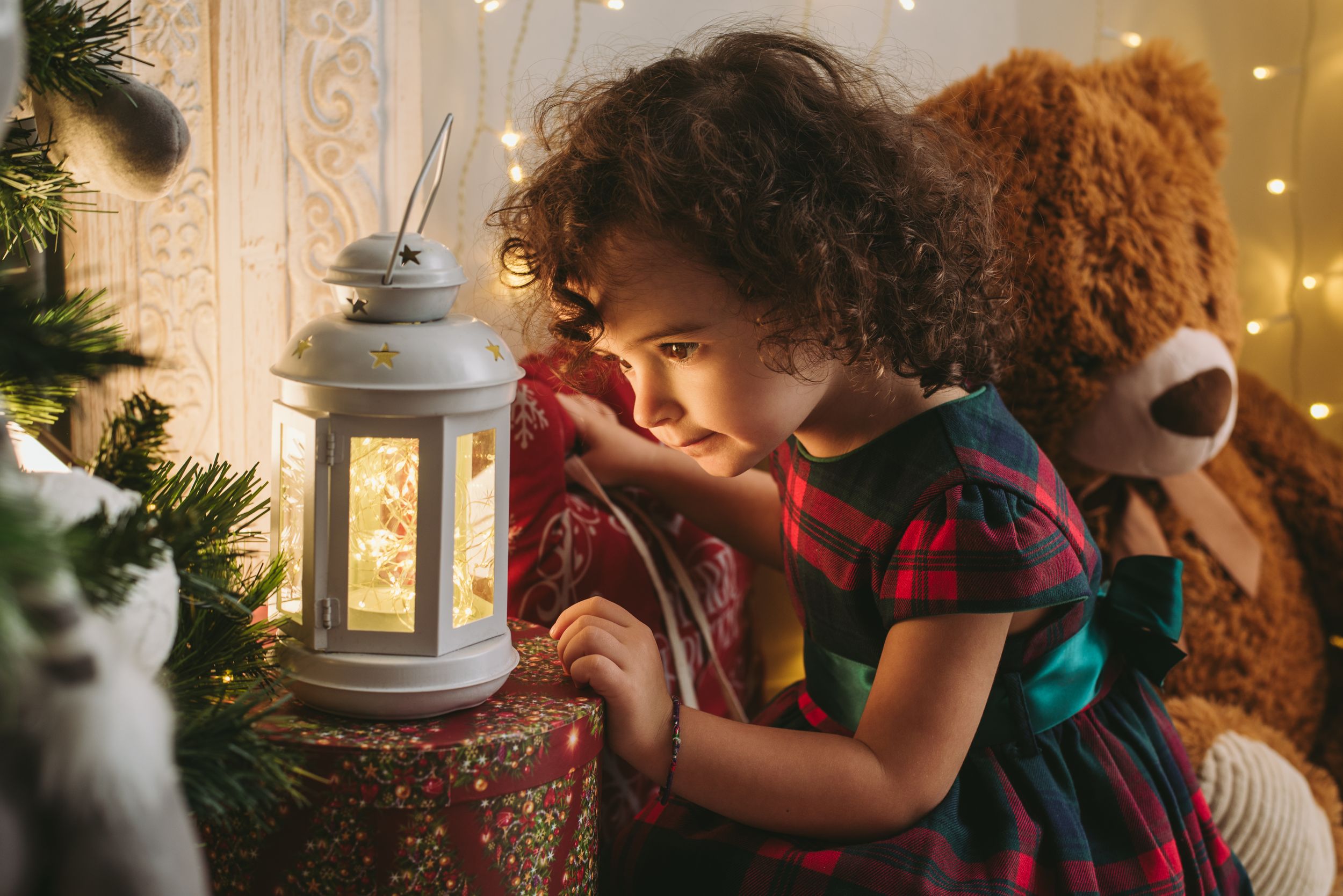 Child looking into glowing white lantern by Christmas decorations.