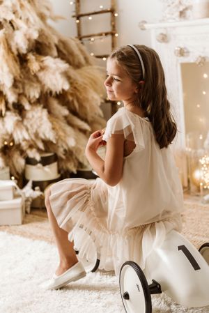 White-dressed figure sitting by decorated Christmas tree with twinkling lights and decorative elements.