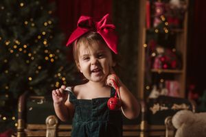 A joyful holiday portrait with a red bow and dark dress against a Christmas tree background.