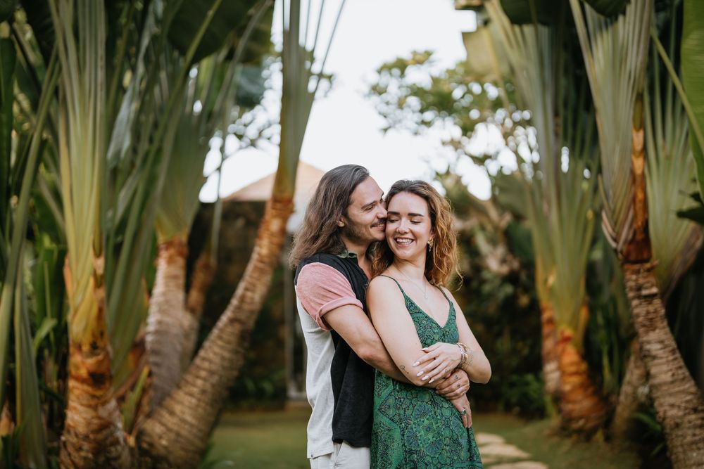 A romantic couple embraces under palm trees in a tropical garden setting during sunset.