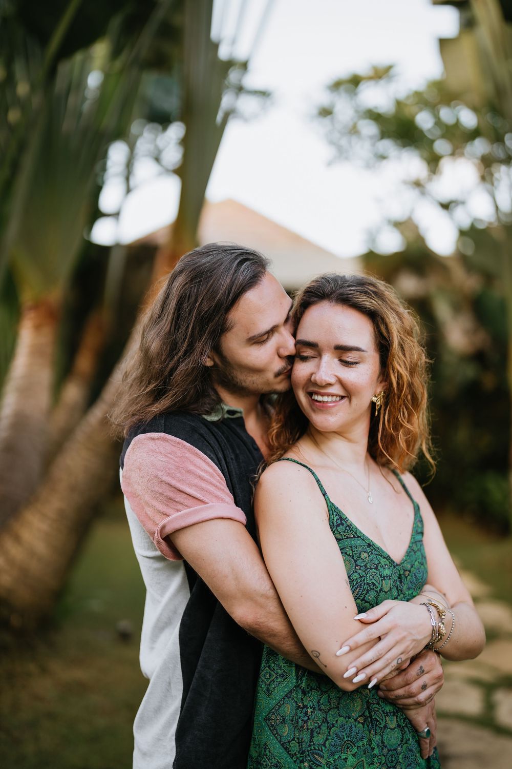 A couple shares laughter and embraces in a garden setting with palm trees.