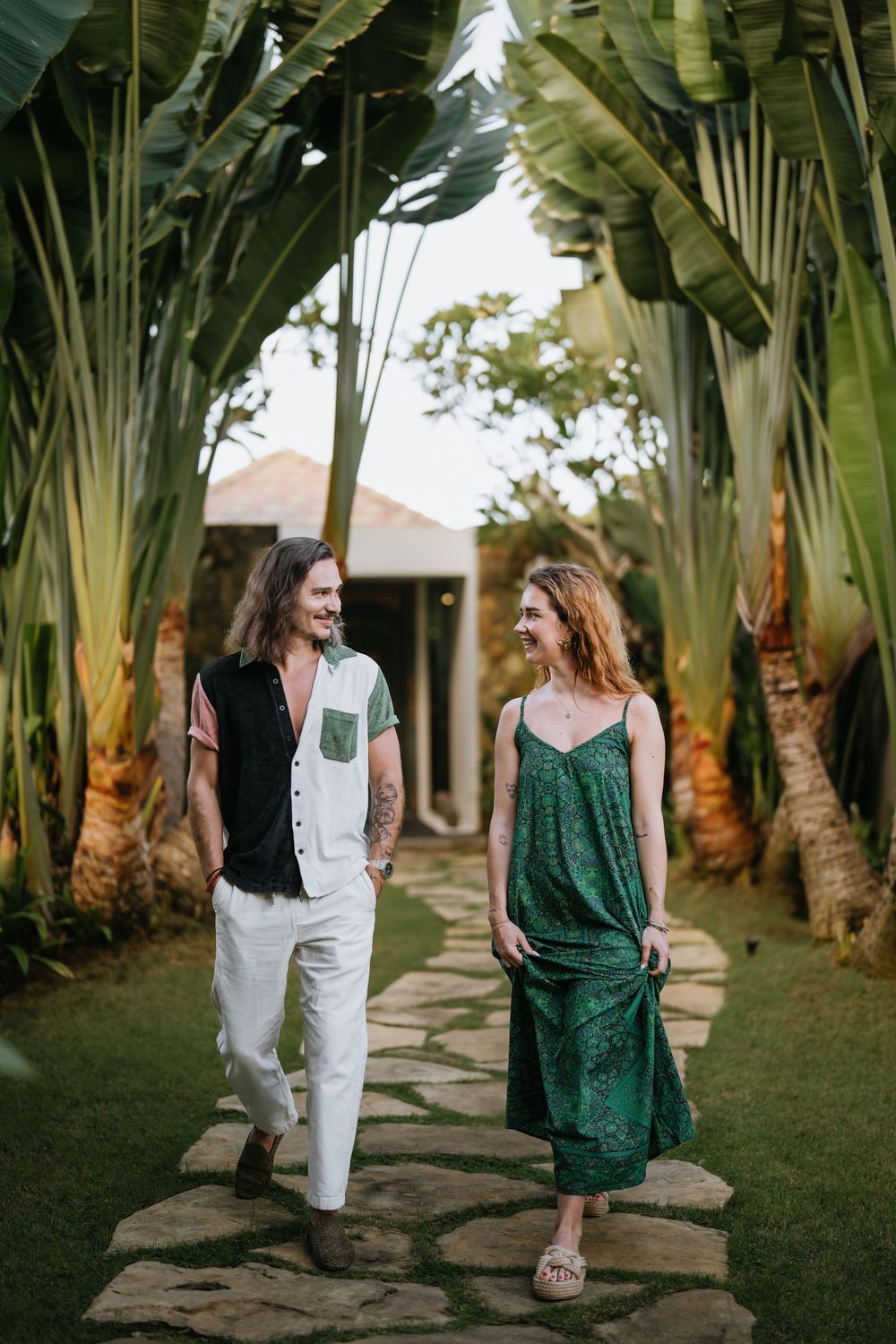 Two people walk together along a stone path surrounded by tropical palm trees.