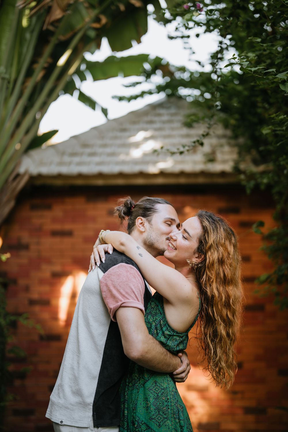A couple shares an intimate moment against a rustic brick wall backdrop in a garden.