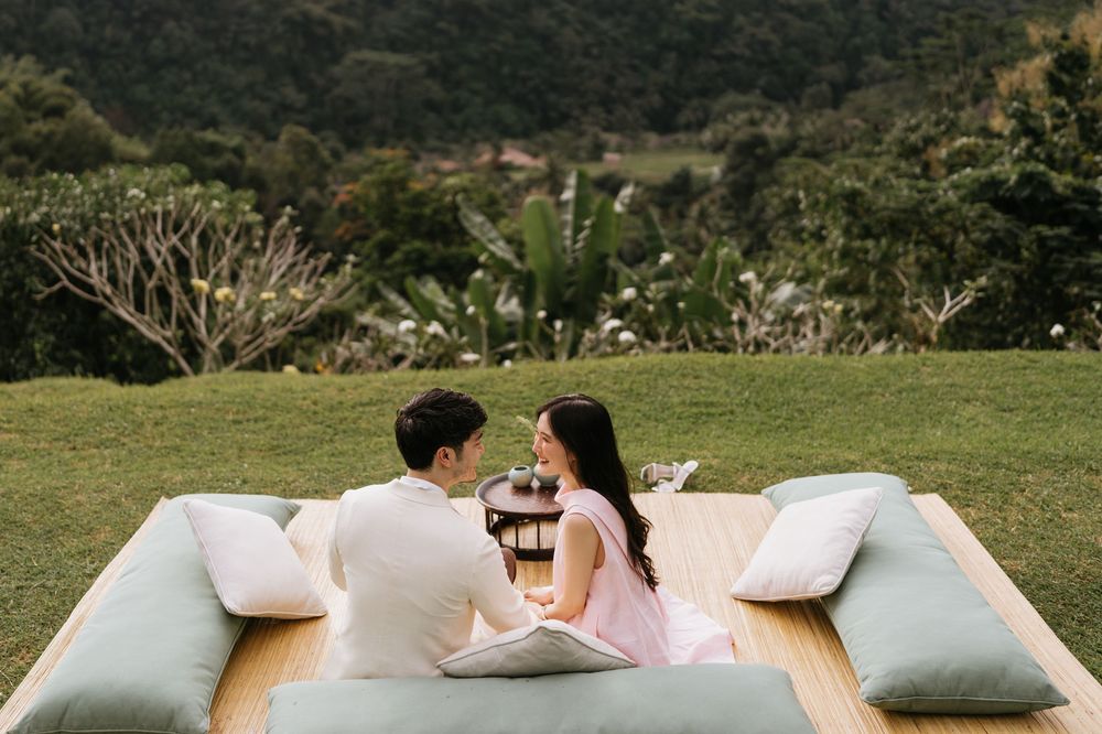 A couple enjoys a romantic outdoor picnic setting with cushions on a grassy lawn.
