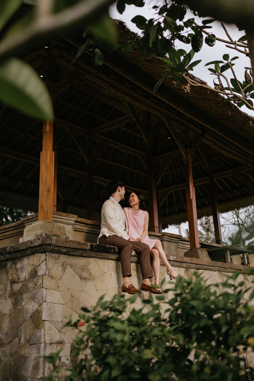 Two people share a quiet moment on a rustic stone gazebo with thatched roof.