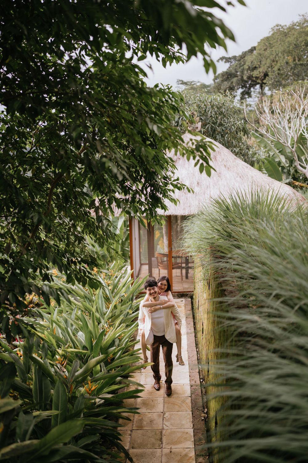 A stone pathway surrounded by lush tropical plants and traditional architecture.