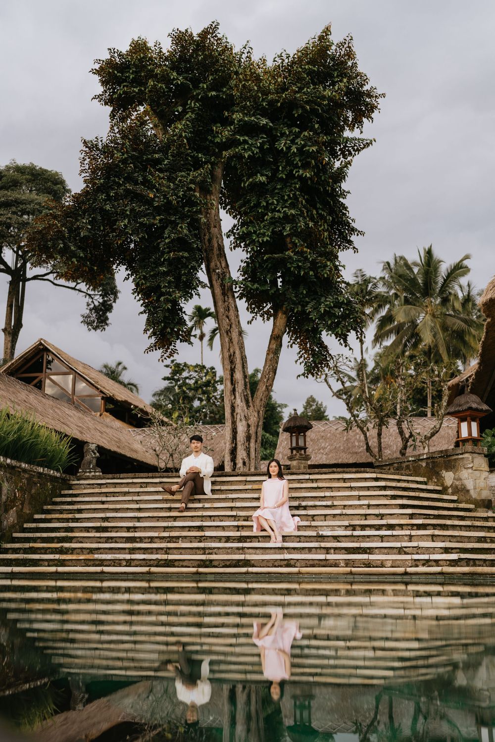 A terraced infinity pool surrounded by trees and traditional Balinese architecture.