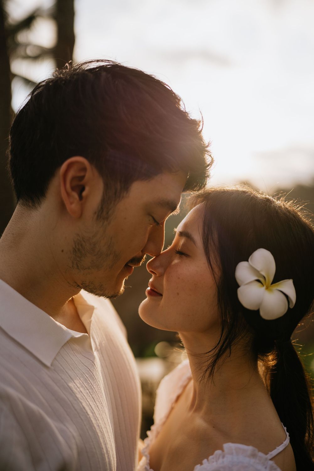 A romantic couple shares an intimate moment at sunset with white flowers in her hair.