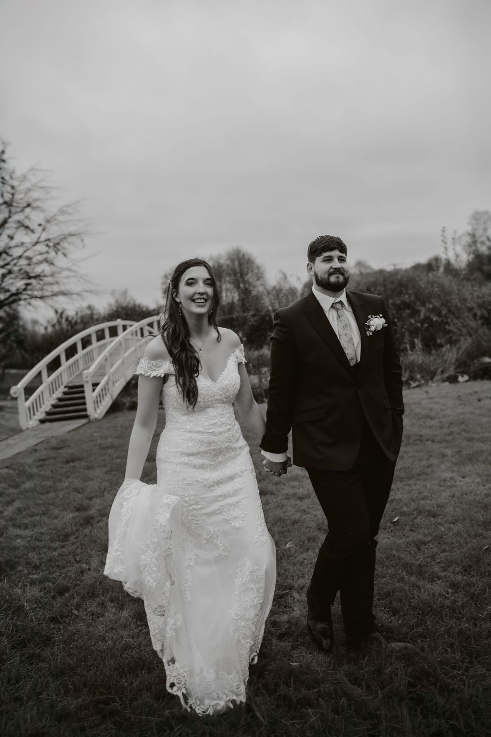 A bride and groom walk together and laugh while posing for black and white wedding photos. Fennes essex wedding photography
