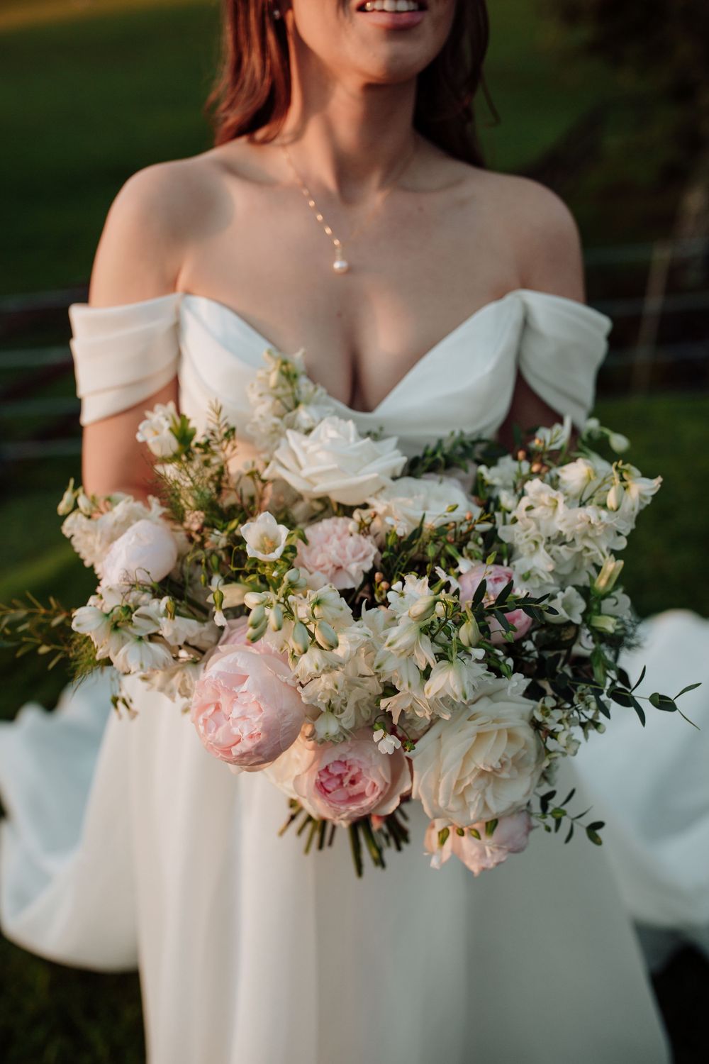 Close-up details of a bride's off-shoulder wedding dress adorned with delicate pink and white floral bouquet arrangements.