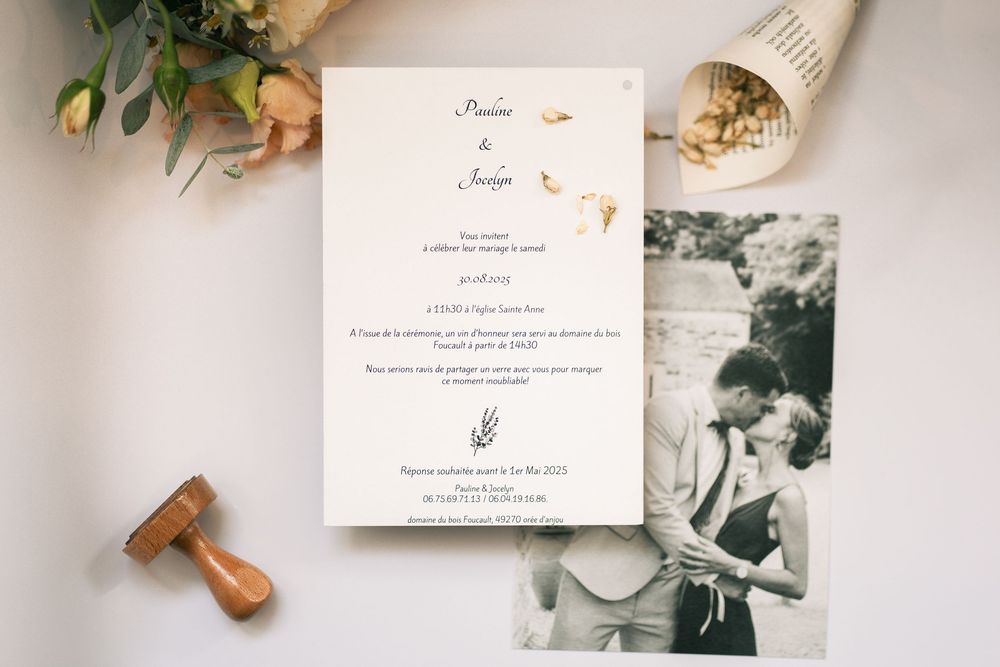 Wedding invitation and vintage photograph displayed with flowers and wooden stamp on white surface.