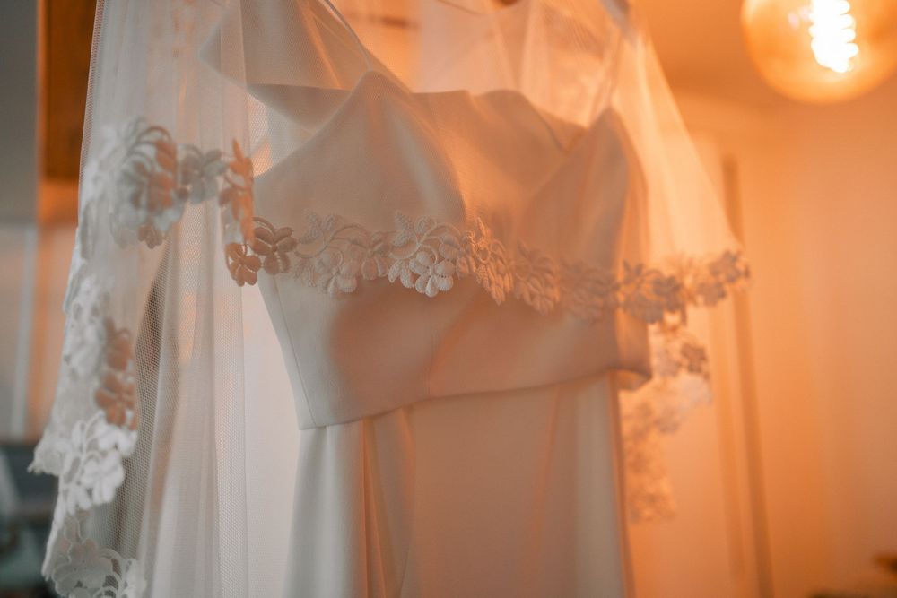 Delicate lace wedding dress details with floral embellishments hanging in warm lighting.