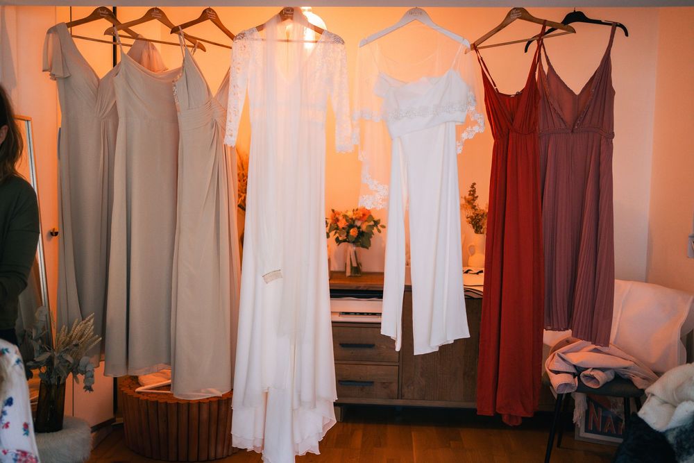 A row of white and pink dresses hanging on wooden hangers in a dressing room.