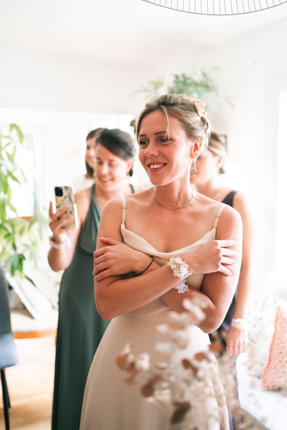 Joyful wedding getting ready moment captured in a bright indoor space with greenery in the background.