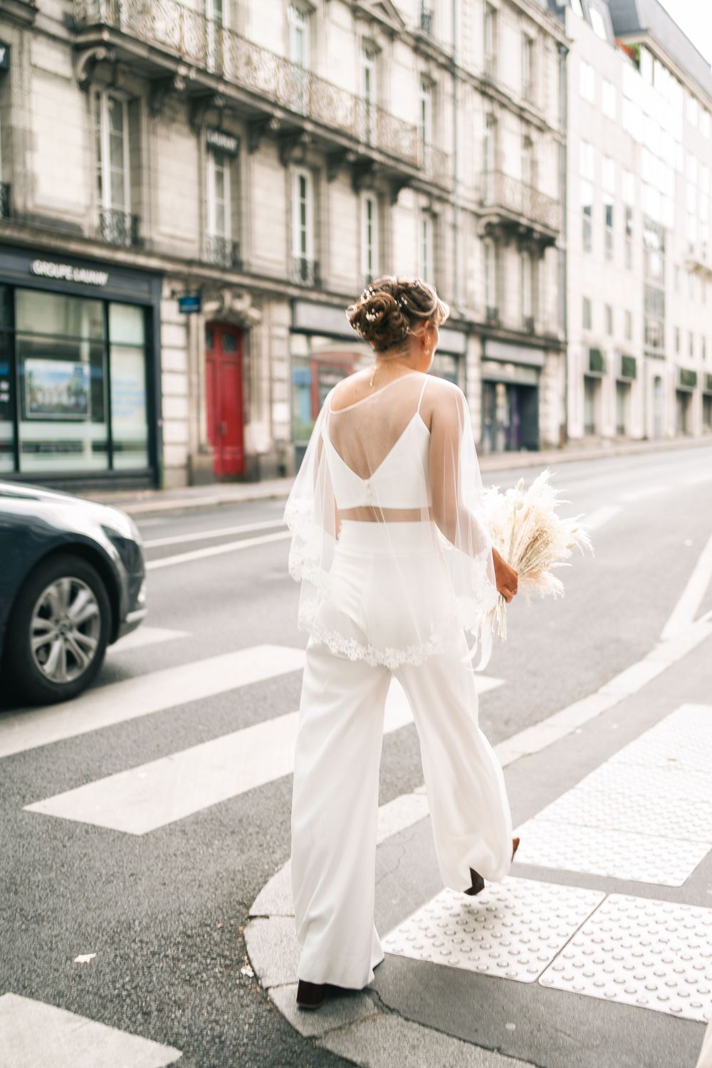 Romantic street scene with flowing white dress against classic Parisian architecture.