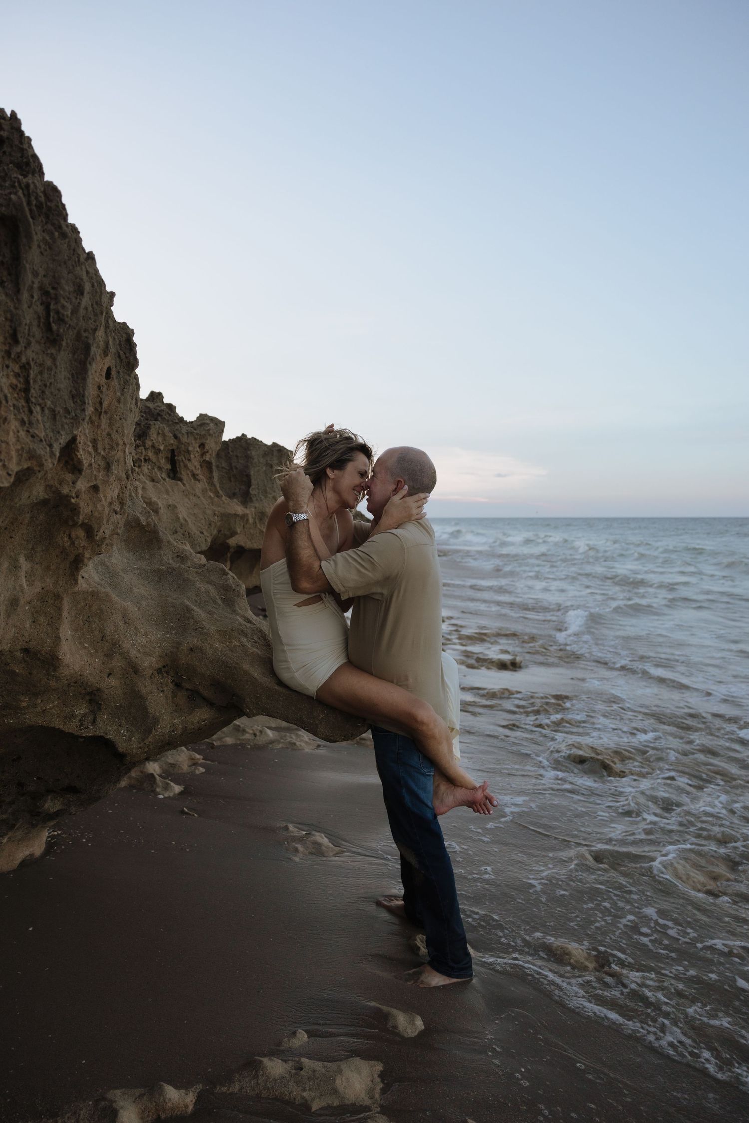 Couple embracing near rocky cliffs on a dramatic beach landscape.