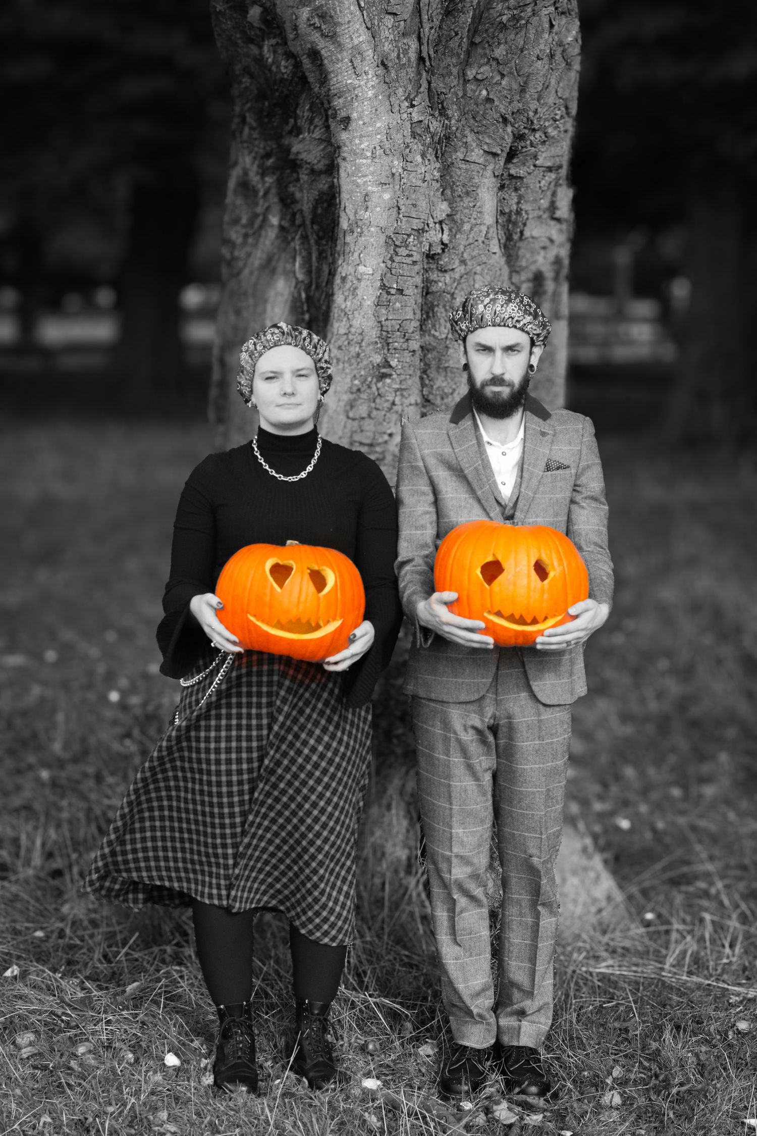 Two carved jack-o'-lanterns held against tree trunks in dramatic black and white composition.