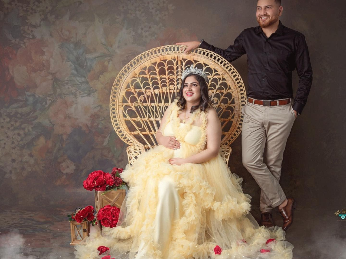 An ornate wicker peacock chair sits amidst scattered red roses with soft studio lighting against a textured backdrop.