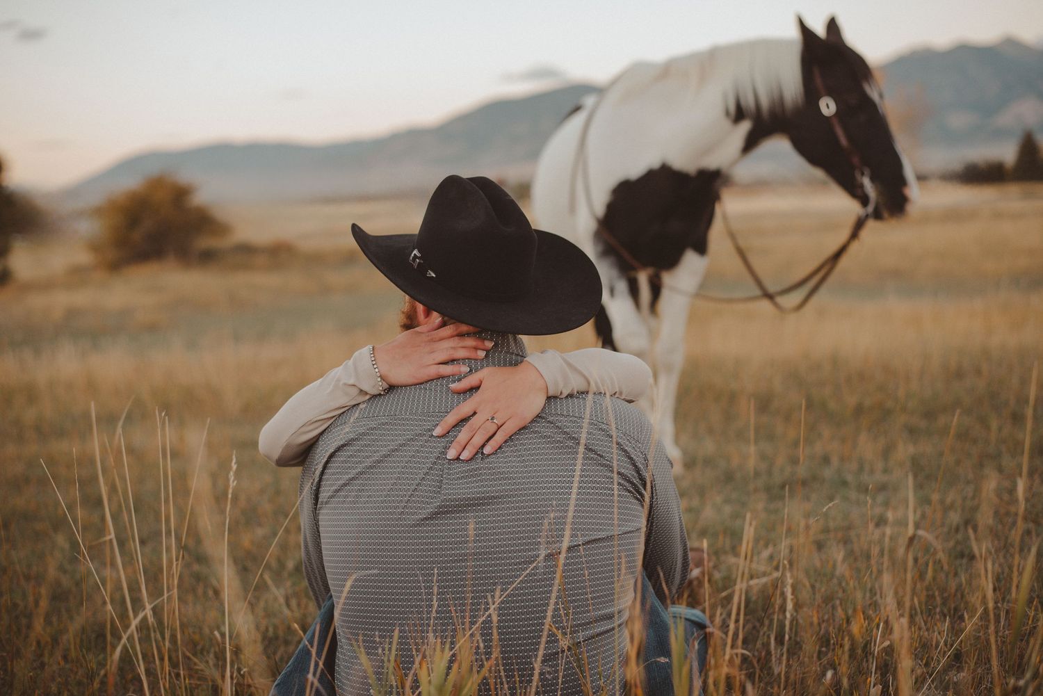 A couple shares a tender moment against a backdrop of mountains and open fields.