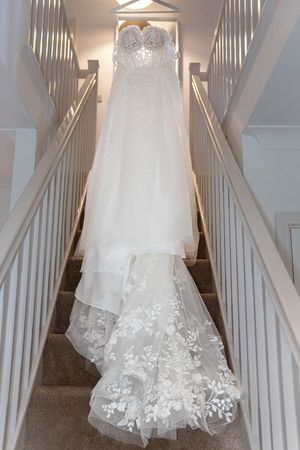 Elegant white wedding dress with lace details hanging on display against a white staircase.