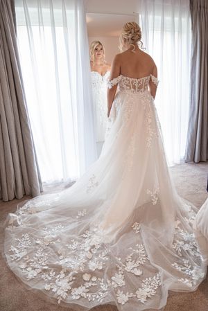 Stunning wedding dress with intricate lace train and floral appliques shown from multiple angles in bridal suite.