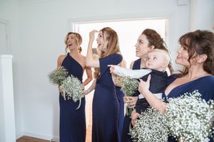 Group of people in navy blue and floral outfits gathered together in a white-walled interior space.