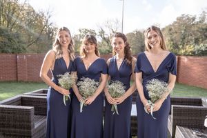 Bridesmaids in navy blue dresses hold bouquets while posing outdoors.