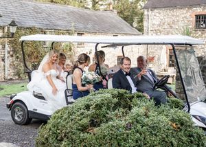Newlyweds ride in a golf cart decorated with greenery at their wedding venue.