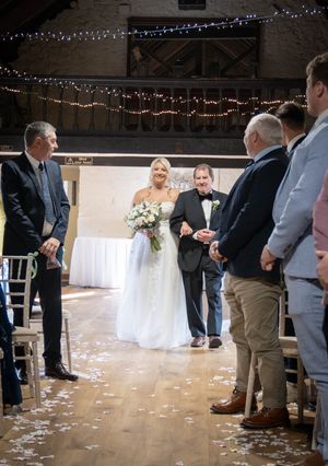Wedding party makes their entrance into a rustic barn reception venue with string lights overhead.