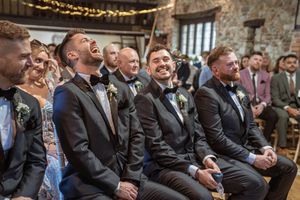 Wedding guests in formal attire laugh and enjoy themselves during the ceremony in a stone-walled venue.